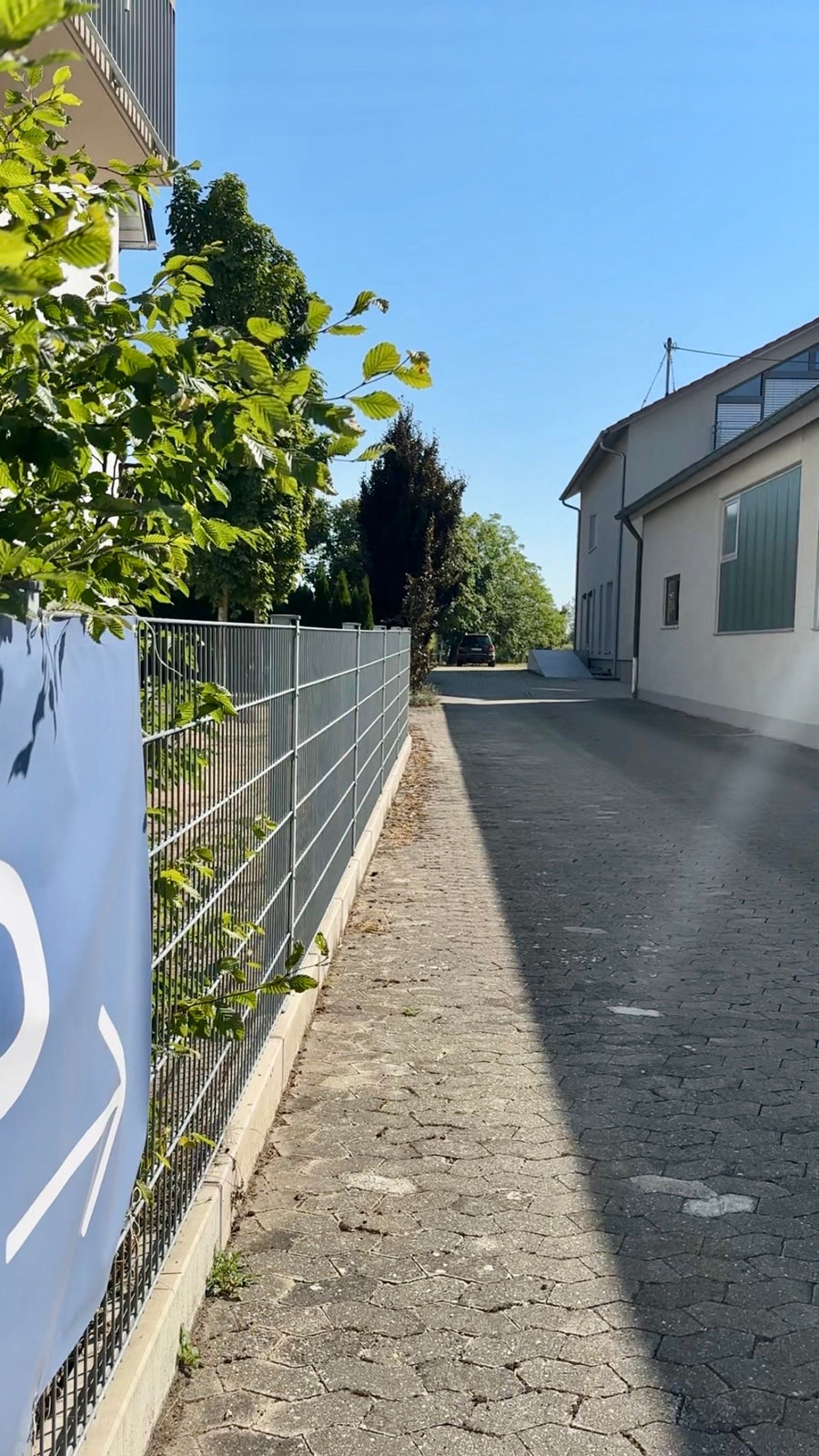 Gepflasterter Weg am Haus entlang, links das Banner mit Pfeil