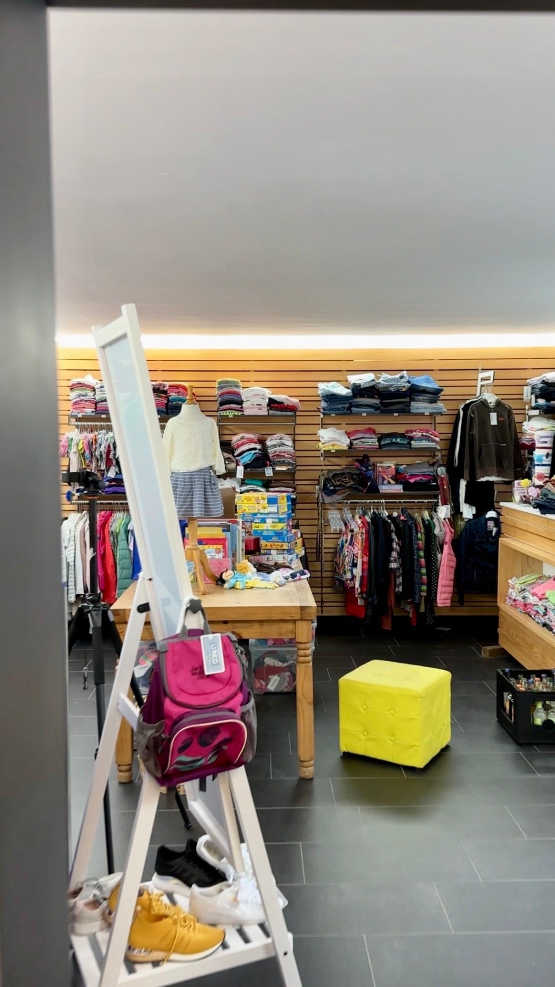 Zweiter Ladenraum mit Holzwand, Spielen, Büchern, Spiegel und Schuhregal