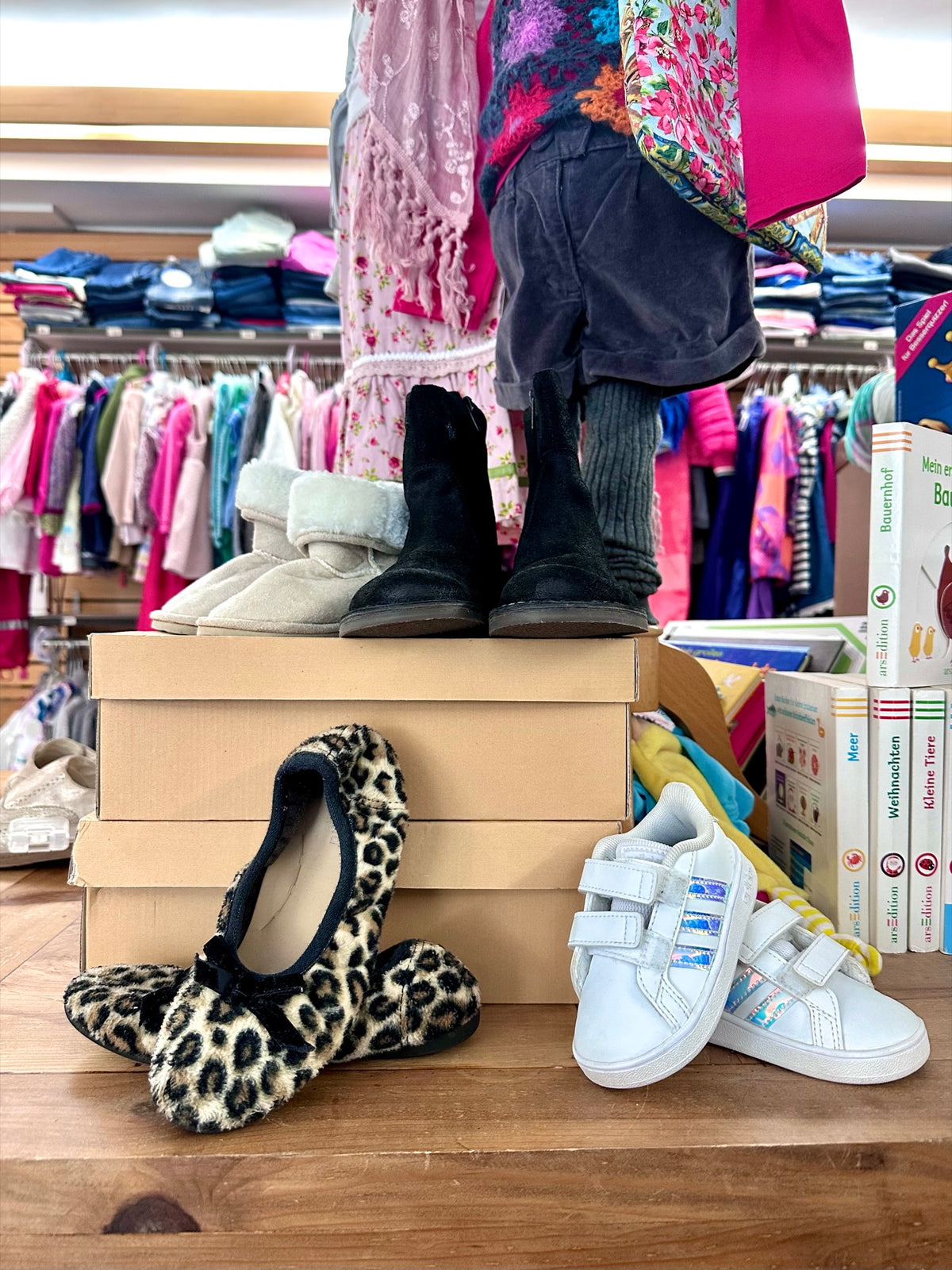 Kinderschuhe und Ballerinas auf Kartons vor Kleiderstangen