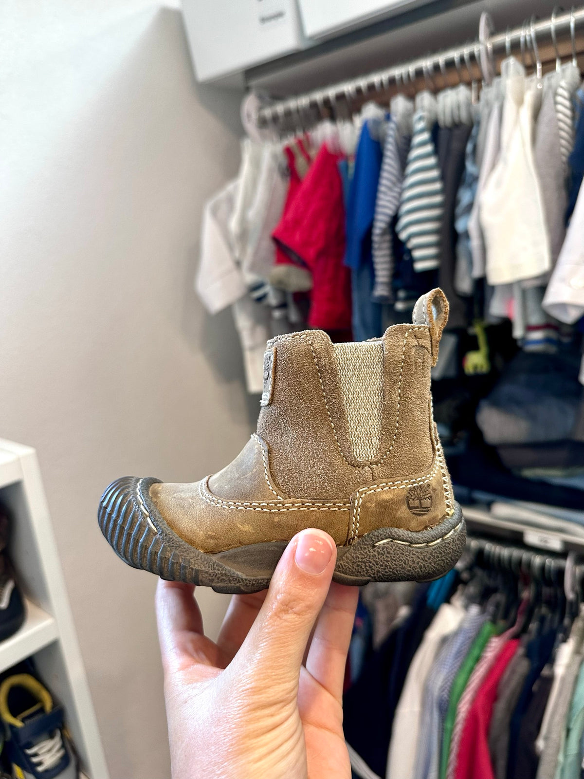 Brauner Kinder-Lederstiefel in der Hand, im Hintergrund Kleiderstangen
